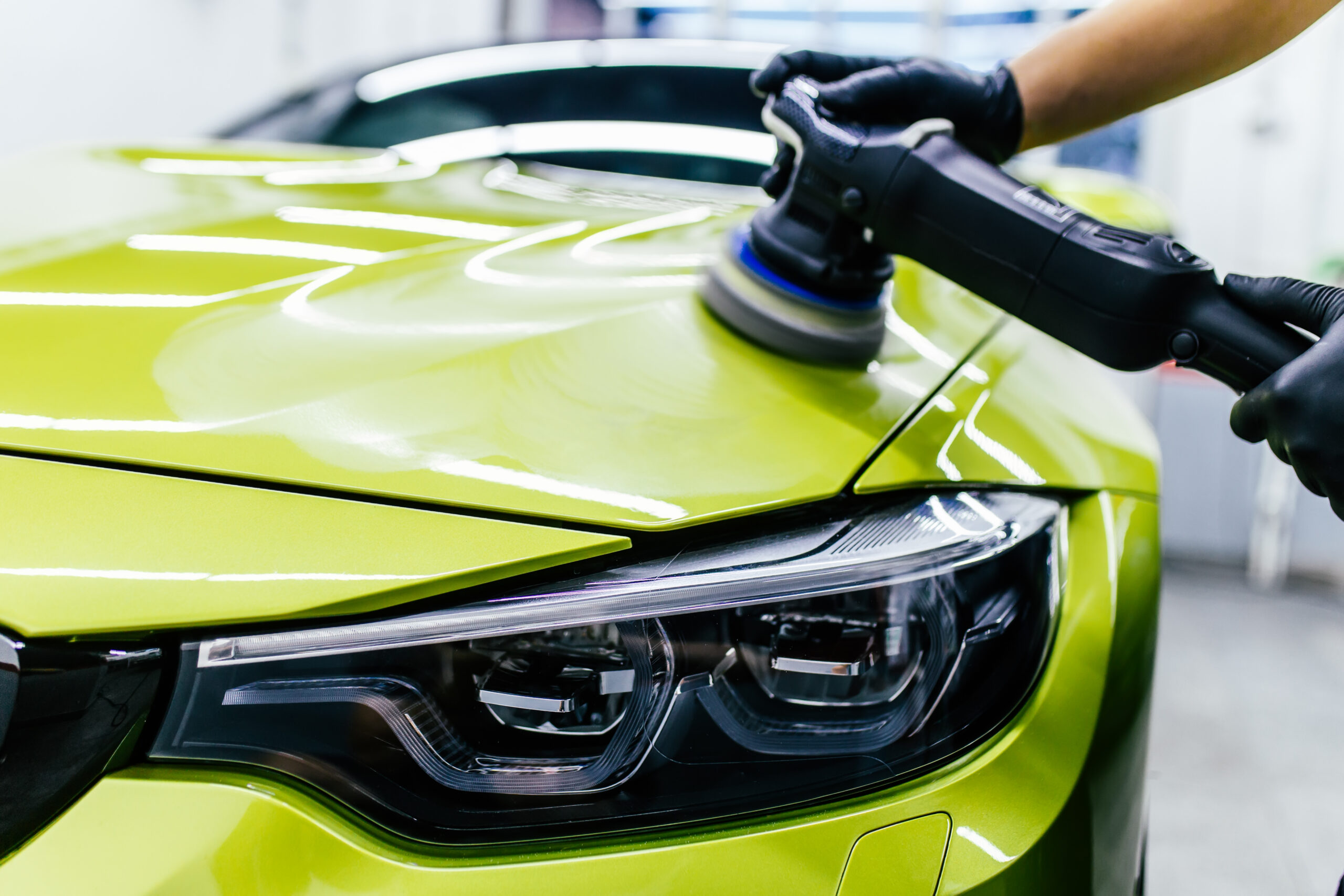 Car detailing Worker with orbital polisher in auto repair shop.
