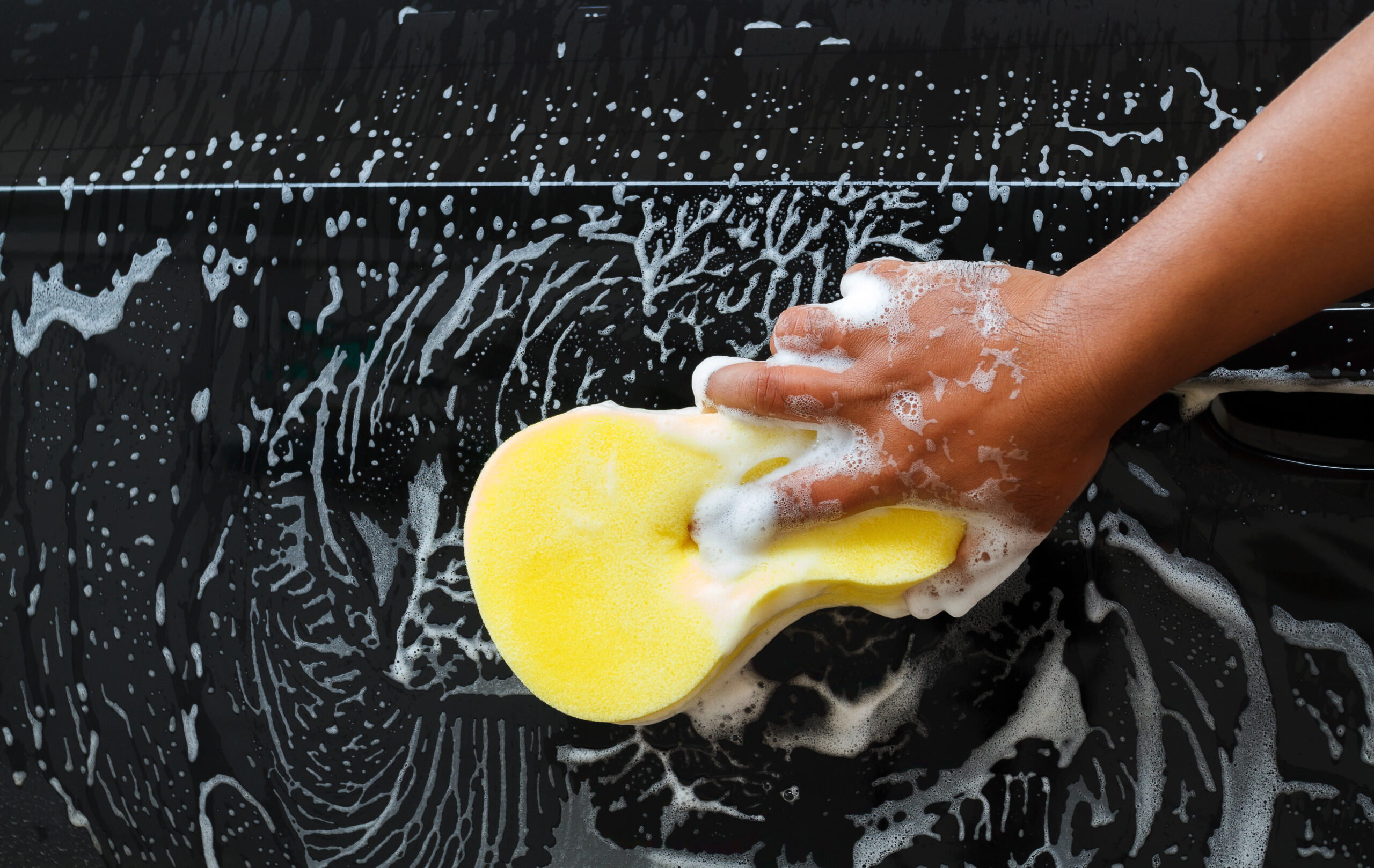 Man washing the car using the yellow sponge with foam .
